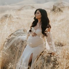 a pregnant woman in a white dress standing next to a rock and looking off into the distance