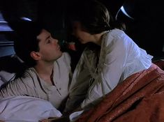 a man and woman laying in bed with one looking at the other's face