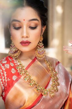 a woman in a red and gold saree holding her hands up to her face