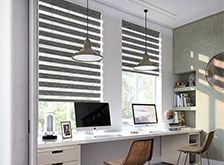 a computer desk sitting under two windows in a room