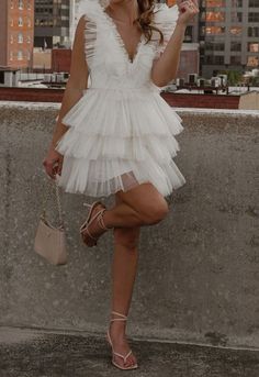 a woman in a short white dress is holding an umbrella and posing for the camera