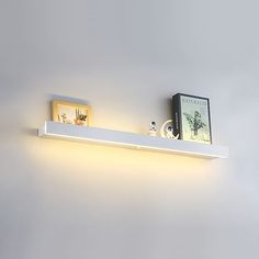 a white shelf with two books on top of it and a light above the shelf