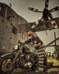 a man in striped pants sitting on a motorcycle next to an old airplane and plane