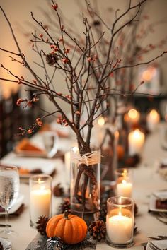 a centerpiece with candles, branches and pumpkins is displayed on a dining room table