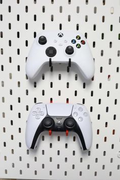 two video game controllers sitting on top of a white pegboard next to each other