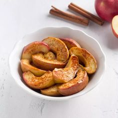 a bowl filled with sliced apples on top of a white counter next to cinnamon sticks