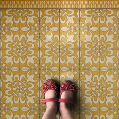 a woman's feet with red shoes standing in front of a yellow and white tile wall