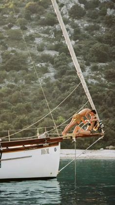 a man and woman are sitting on a sailboat in the water with trees behind them