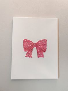 a pink bow on a white card with some glitter in the middle, hanging on a wall