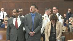 two men in suits and ties standing next to each other at a courtroom with police officers behind them