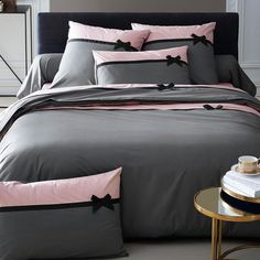 a bed with grey and pink sheets and pillows