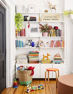 a white book shelf filled with lots of books next to a chair and potted plant