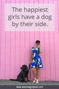 a woman standing in front of a pink wall with a black dog sitting next to her