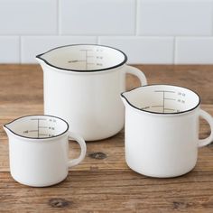 three white measuring cups sitting on top of a wooden table