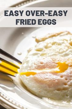 an egg is being fried on a white plate with yellow utensils in front of it