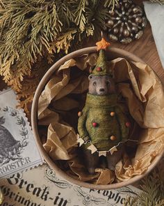 a small stuffed animal in a wooden bowl surrounded by christmas decorations and pine cones on the table