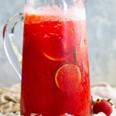 a pitcher filled with liquid sitting on top of a table next to some strawberries