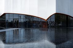 the reflection of two curved glass windows in front of a building with water reflecting on it