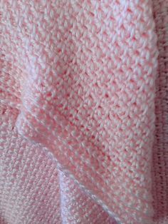 a pink and white knitted blanket on top of a bed