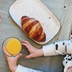 a person holding a glass of orange juice next to a croissant