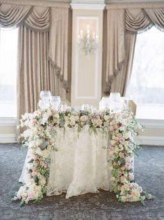 a table with flowers and candles on it in front of a chandelier filled with curtains