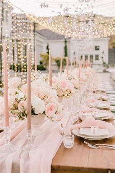 a long table is set with pink and white flowers, candles, and napkins