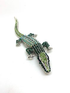 an alligator brooch with green and blue beads on it's back end, sitting on