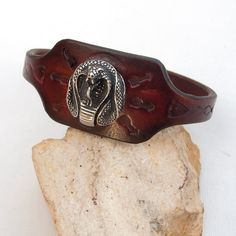 Made from top quality vegetable tanned leather. Hand painted, stamped, antiqued leather cuff bracelet for men. With antique silver Cobra head screw Cobra head sizes: Length; 2.2 cm Width; 2.5 cm  Cuff is 1,33 inches (3,4 cm) wide Sizing (choose at checkout) Please look at my other bracelets! For example this: https://www.etsy.com/listing/253535448/men-leather-cuff-bracelet-tribal-dyed?ref=shop_home_active_1 FEDEX to USA, Canada and Australia! If you need a faster shipping please use this service Vintage Leather Bracelet With Engraving, Vintage Engraved Leather Bracelets, Adjustable Brown Engraved Cuff Bracelet, Vintage Leather Concho Bracelets, Adjustable Carved Cuff Bangle Bracelet, Adjustable Carved Cuff Bangle, Vintage Leather Engraved Bracelet, Vintage Leather Bracelet With Concho, Vintage Hand Tooled Bracelets For Festivals