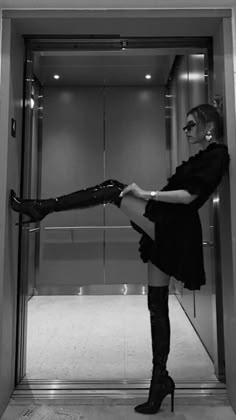 a woman standing in an elevator with her legs up and wearing high heeled boots