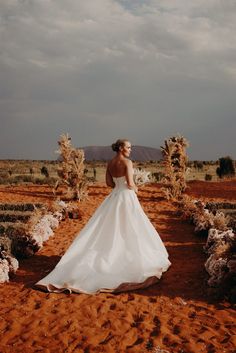 a woman in a white wedding dress standing in the middle of an open desert area