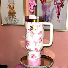 a pink and white coffee cup sitting on top of a metal tray in front of pictures