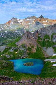 a blue lake surrounded by mountains under a cloudy sky with snow on the top and bottom