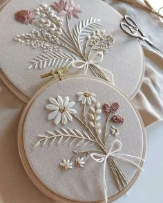 three embroidery hoops with flowers on them sitting on top of a cloth covered table