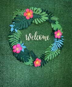 a welcome sign made out of paper with pink flowers and green leaves on the grass