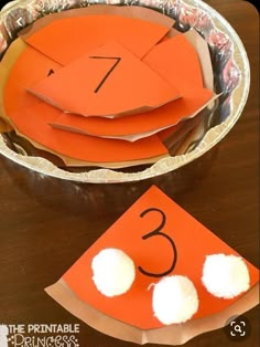 paper plates with numbers and pom poms on them sitting on a wooden table