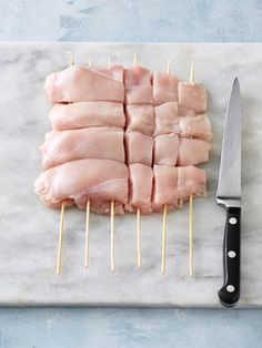 sliced chicken on toothpicks with a knife next to it