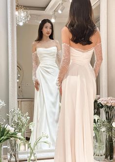 a woman is looking at herself in the mirror wearing a wedding dress with long sleeves