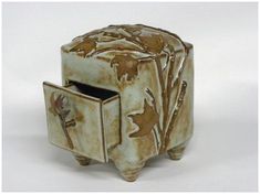 a small ceramic box with a cross on the front and an open drawer in the middle