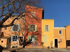 an orange building with green shutters and trees in the foreground on a sunny day