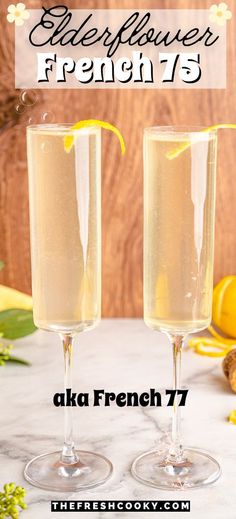 two glasses filled with liquid sitting on top of a table next to lemons and flowers