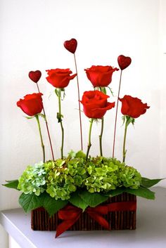 red roses are arranged in a basket with greenery and hearts on the top, along with green leaves