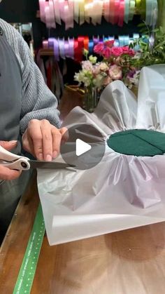 a person cutting paper with scissors on top of a wooden table in front of flowers