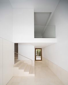 an empty white room with stairs leading up to the second floor and a glass door