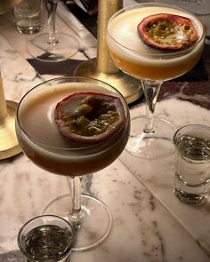 two glasses filled with drinks sitting on top of a marble table next to each other