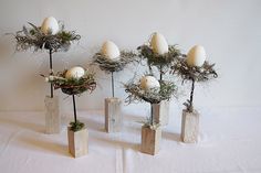 four vases with eggs in them sitting on a white tablecloth covered table cloth