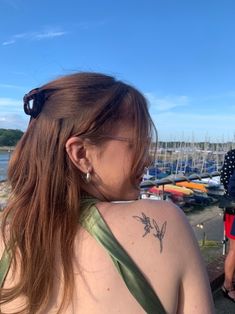 a woman with a tattoo on her back standing in front of a body of water