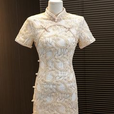 Introducing the stunning short sleeves white lace qipao with delicate floral appliques and faux pearls, a true masterpiece in traditional Chinese fashion. This gorgeous dress is crafted from high-quality lace material that feels soft and comfortable against the skin.The dress features intricate floral appliques that are intricately sewn onto the fabric, creating a beautiful and intricate design that is both feminine and elegant. Faux pearls are also incorporated into the design, adding a touch o Elegant Embroidered Cheongsam For Spring, Traditional White Cheongsam With Stand Collar, Traditional Beige Lace Dress, Elegant Floral Embroidered Dress With Stand Collar, Elegant Embroidered Cheongsam With Stand Collar, Elegant White Cheongsam For Spring, White Fitted Cheongsam With Stand Collar, Elegant Embroidered Ao Dai For Summer, Elegant Floral Embroidered Ao Dai For Summer