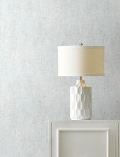 a white table lamp sitting on top of a cabinet next to a wallpapered wall