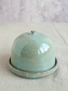 a ceramic covered dish sitting on top of a white tablecloth with a silver ring around it