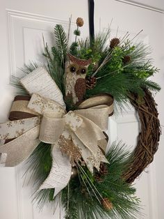 a wreath with an owl and pine cones hanging from the front door, decorated with burlap ribbon